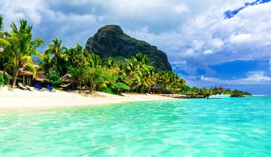Majestic Mauritius Tropical beach in Mauritius with turquoise lagoon, white sand, palm trees, and dramatic mountain peak under blue sky